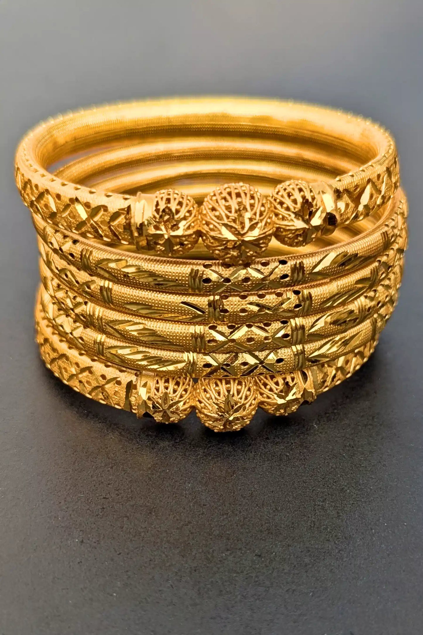 Set of gold bangles with intricate designs on a dark background