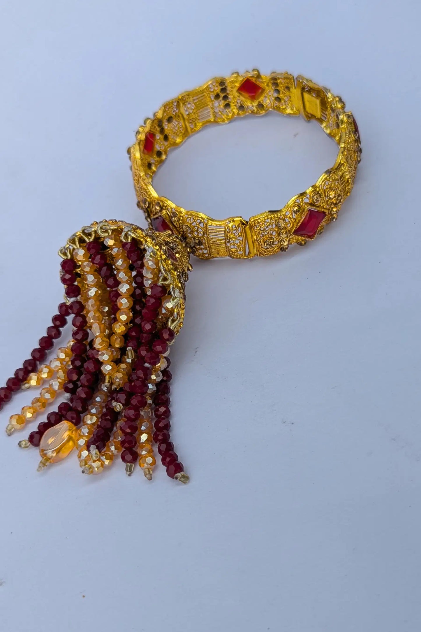 Gold bracelet with red and yellow beads on a white background