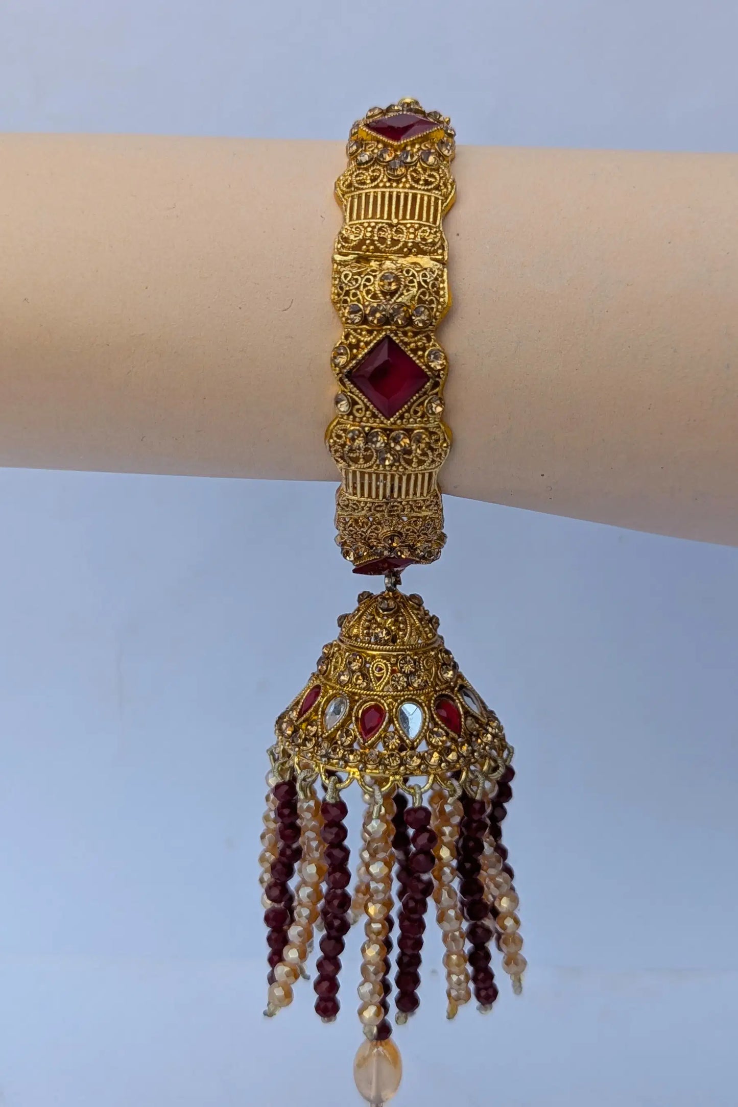 Decorative gold bracelet with red stones and beads on a mannequin arm against a light blue background