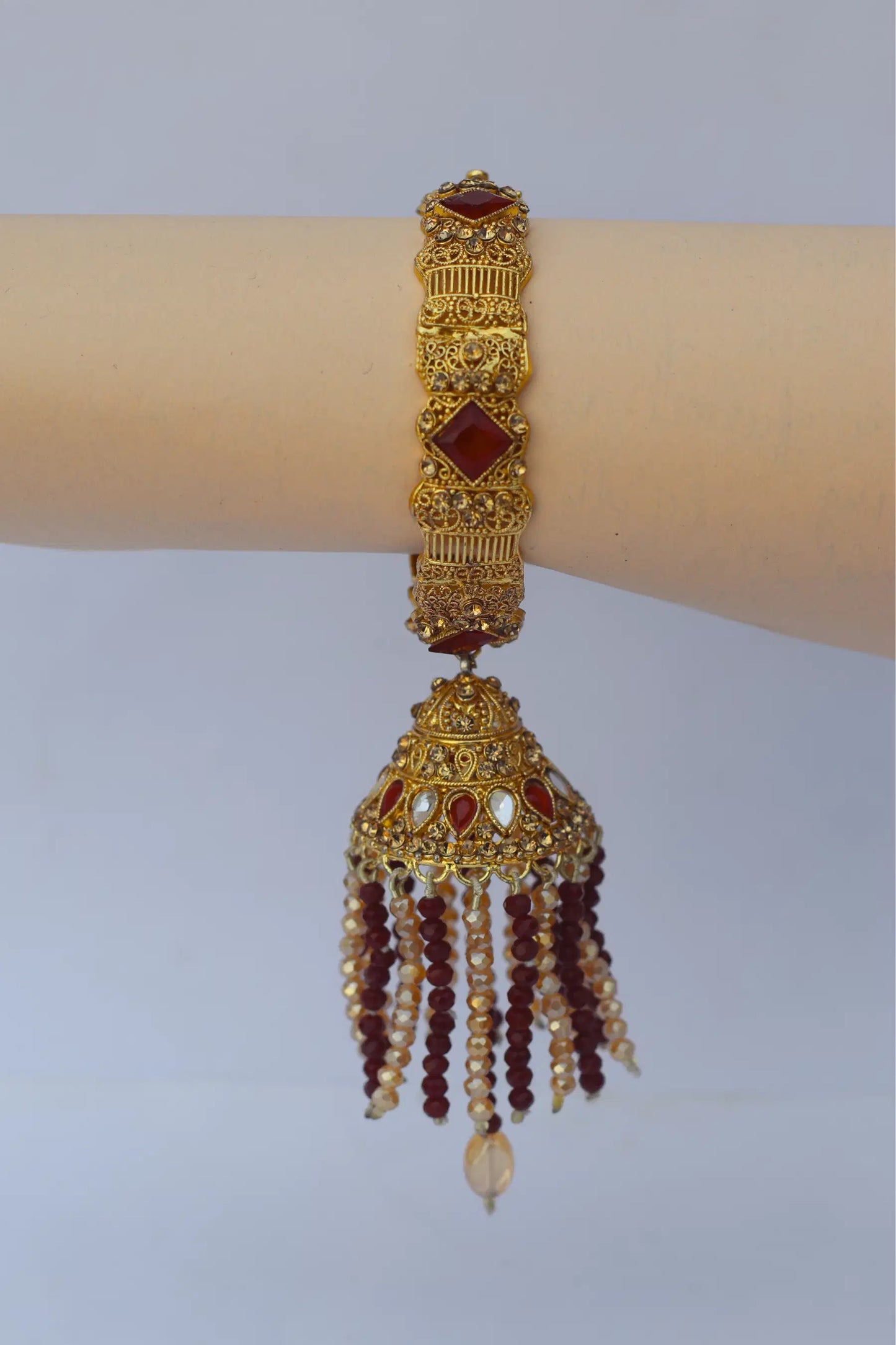 Gold bracelet with red stones on a mannequin arm against a light gray background
