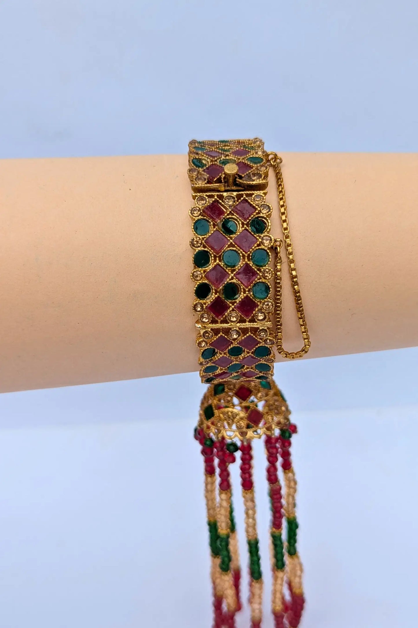 Decorative bracelet with gemstones and beads on a wrist against a light blue background