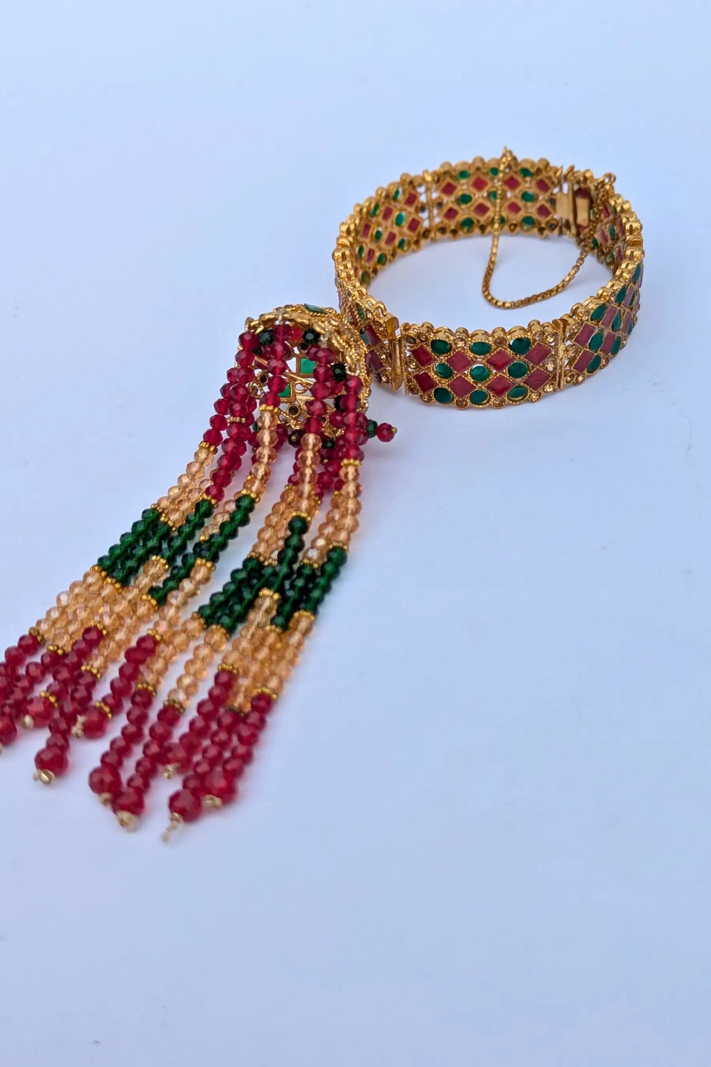Gold bracelet with red and green beads on a light blue background