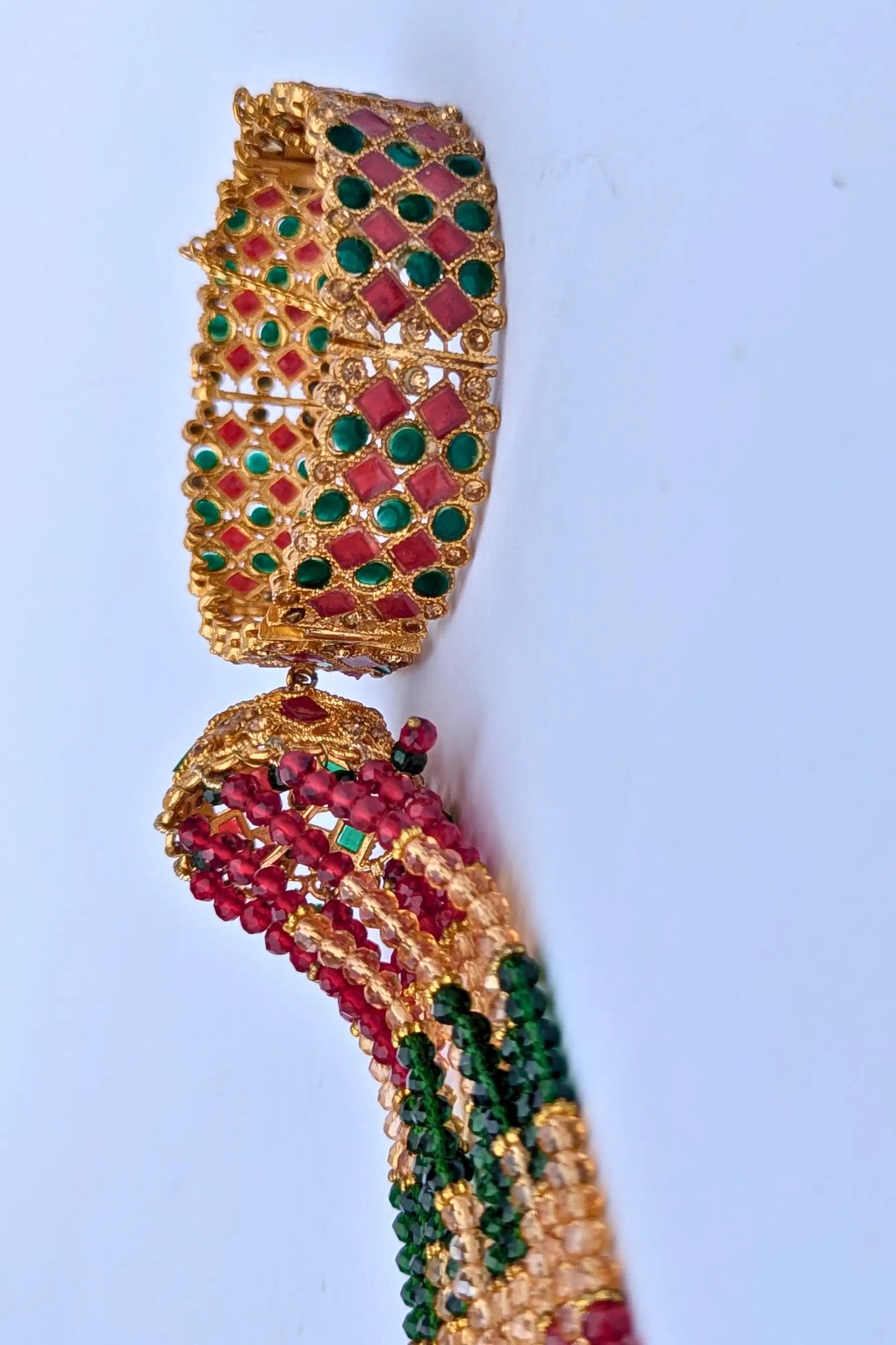 Decorative bracelet with green and red stones on a light blue background