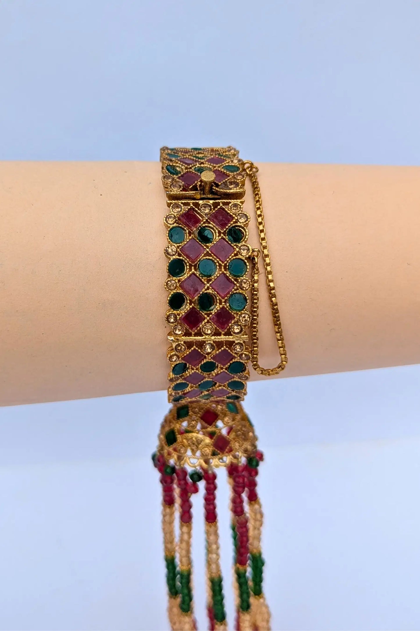 Decorative bracelet with gemstones on a wrist against a light blue background