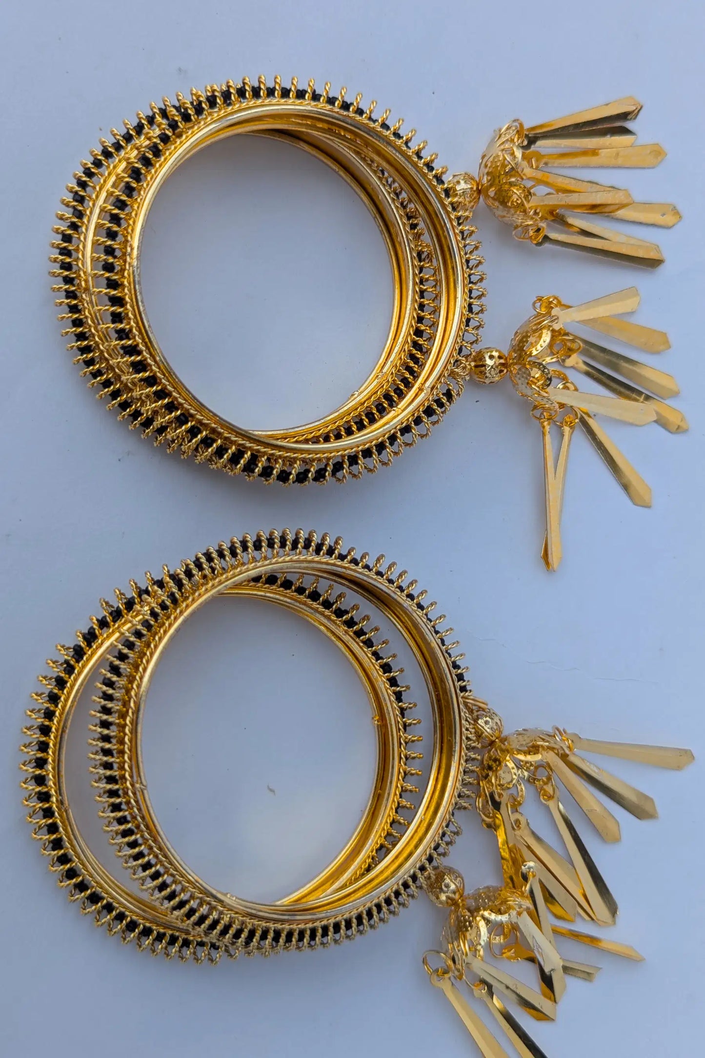 Pair of gold hoop earrings with fan-shaped drops on a light blue background