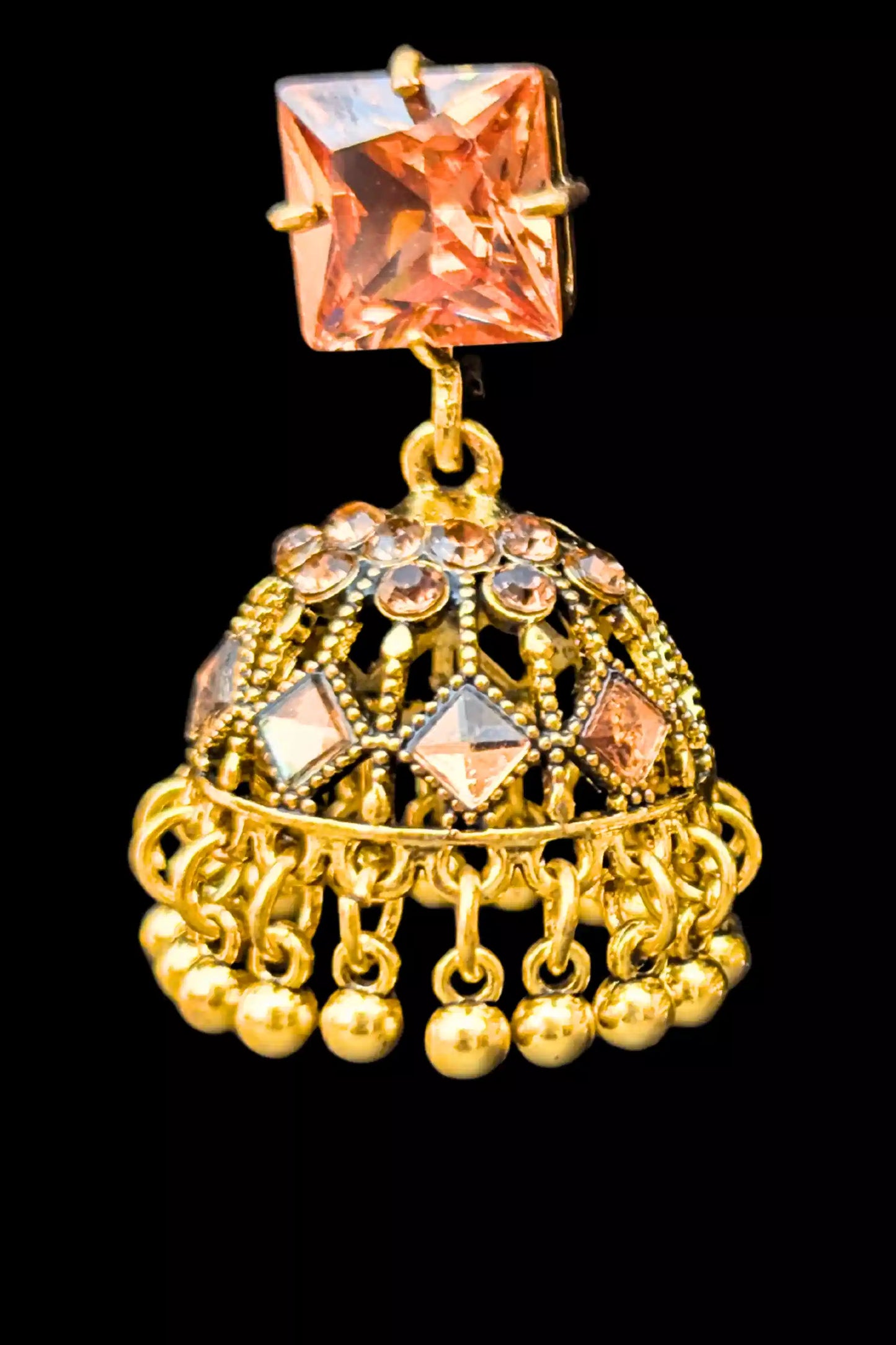 Gold jhumka earring with pink gemstone on a black background
