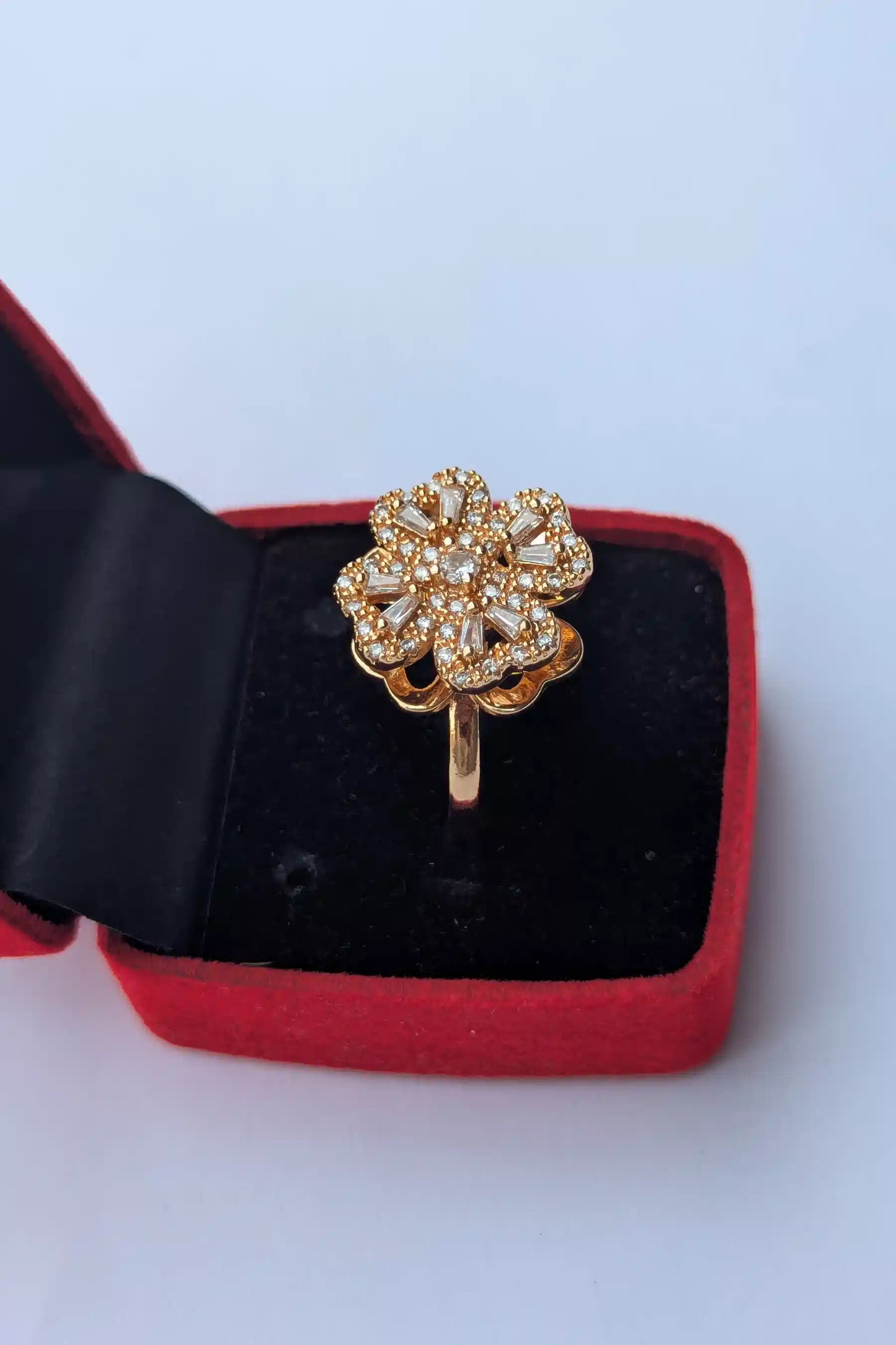 Gold ring with floral design in a red and black jewelry box on a light blue background