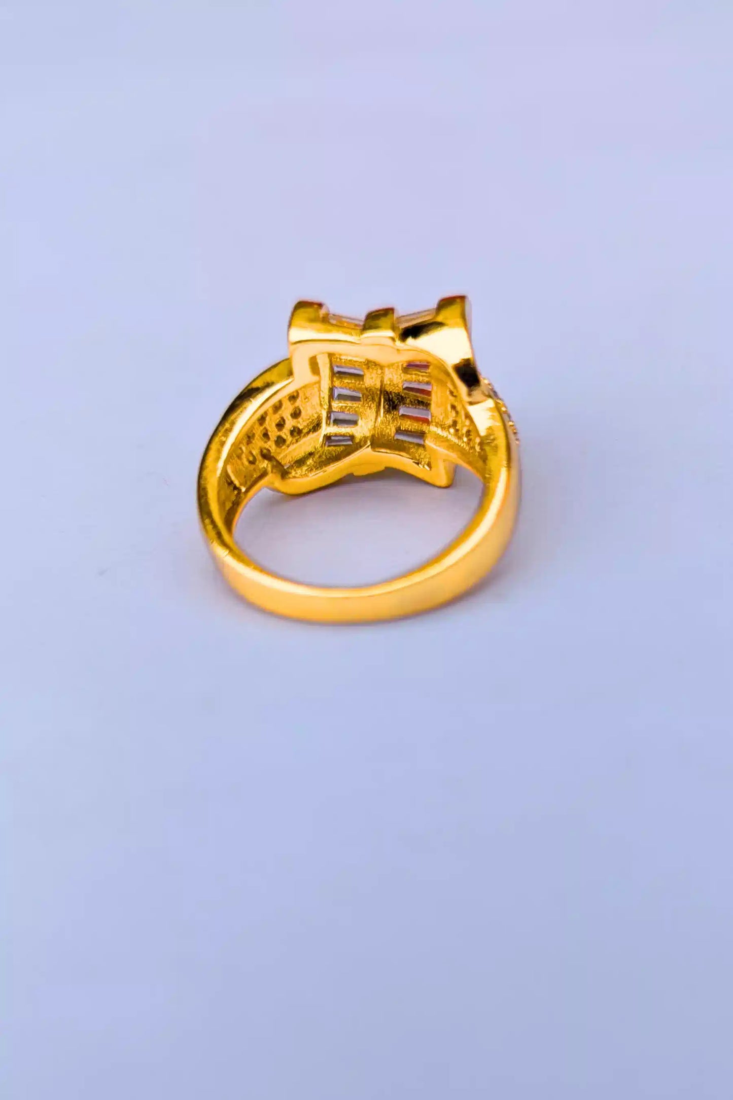 Gold ring with intricate design on a light purple background