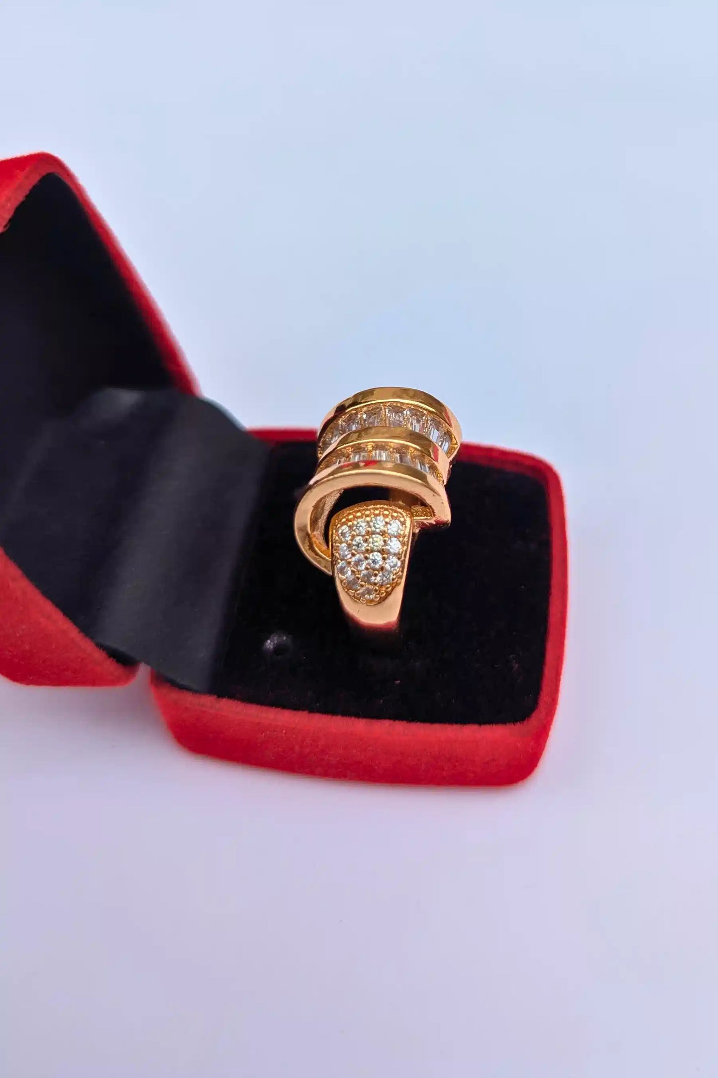 Gold ring with diamonds in a red jewelry box on a light blue background