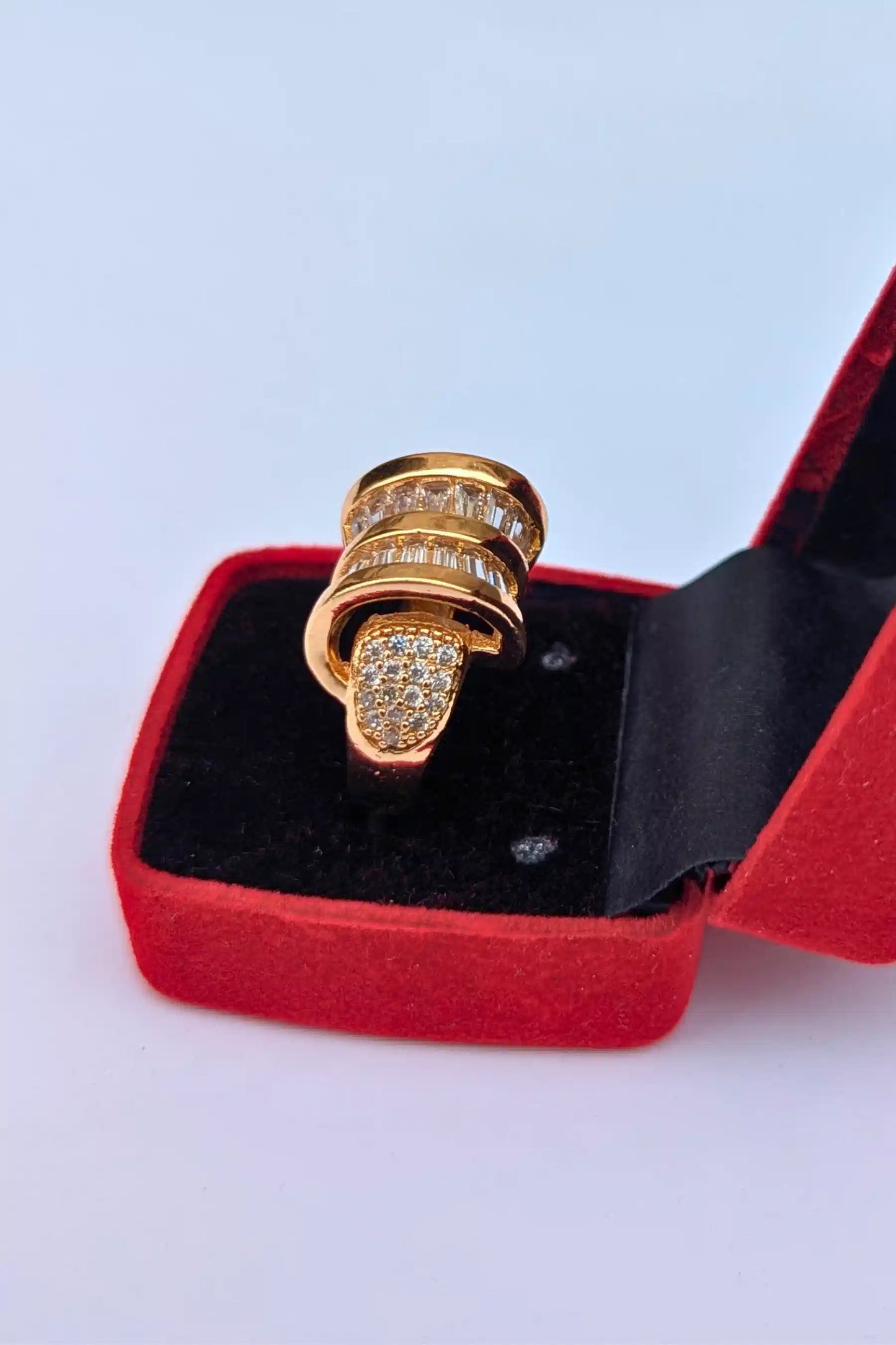 Gold ring with diamonds in a red jewelry box on a light gray background