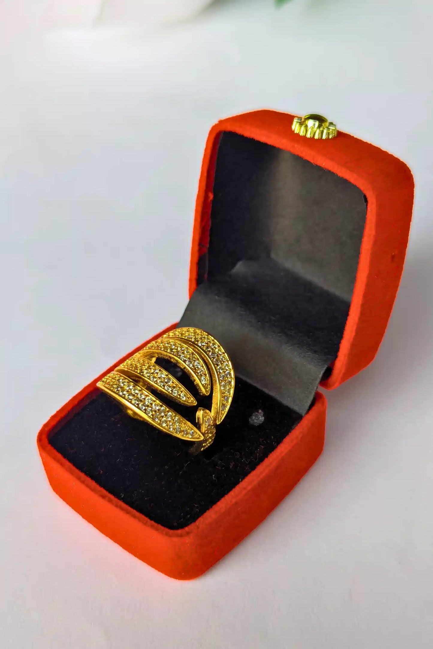 Gold ring with gemstones in an open red jewelry box on a white background
