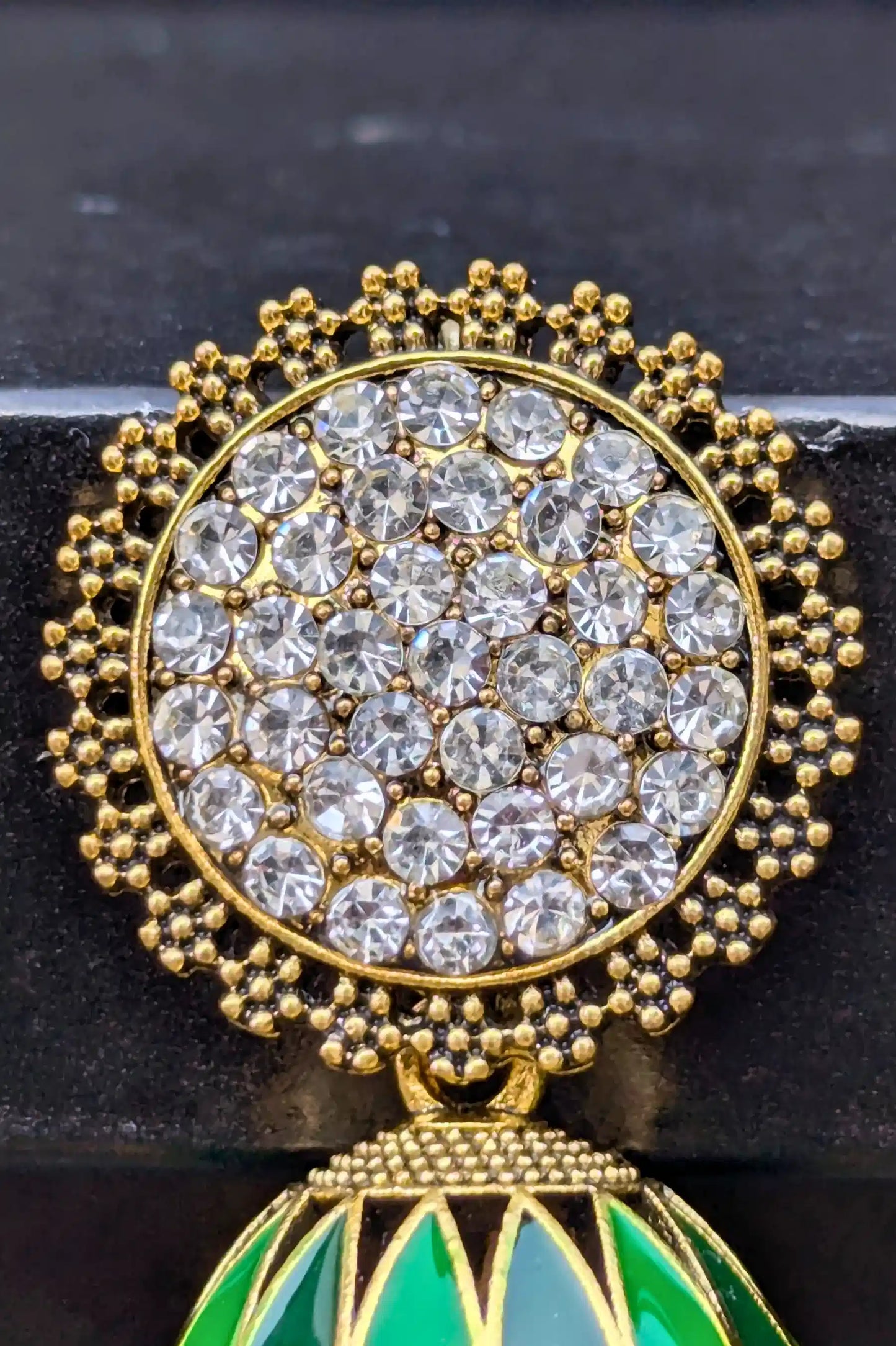 Gold and crystal brooch with green element on a black background