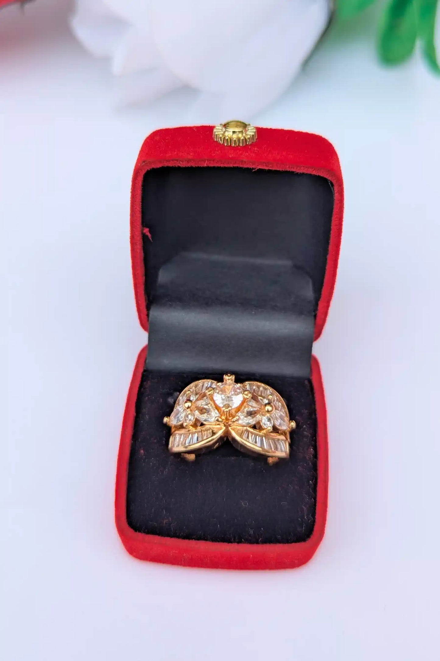 Gold ring with gemstones in a red jewelry box on a white background