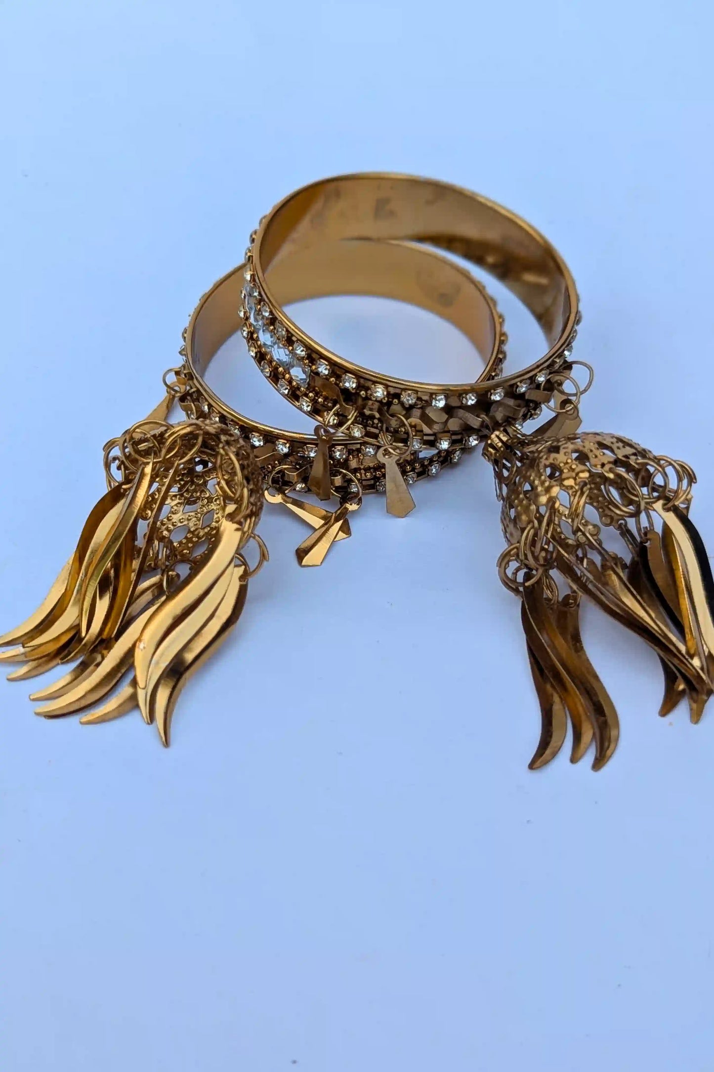 Gold bracelet with fringe details on a light blue background