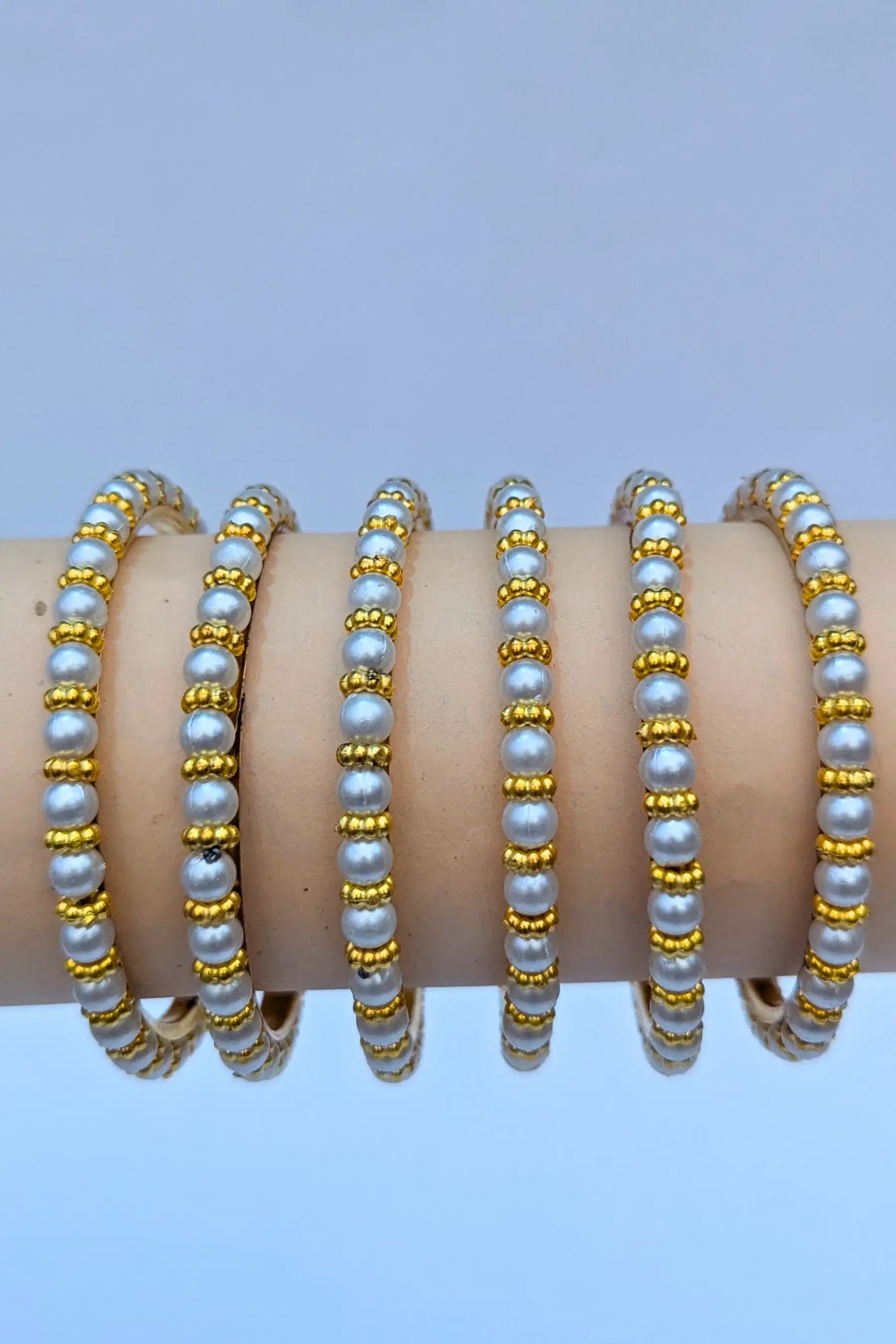 Set of pearl and gold beaded bracelets on a light blue background