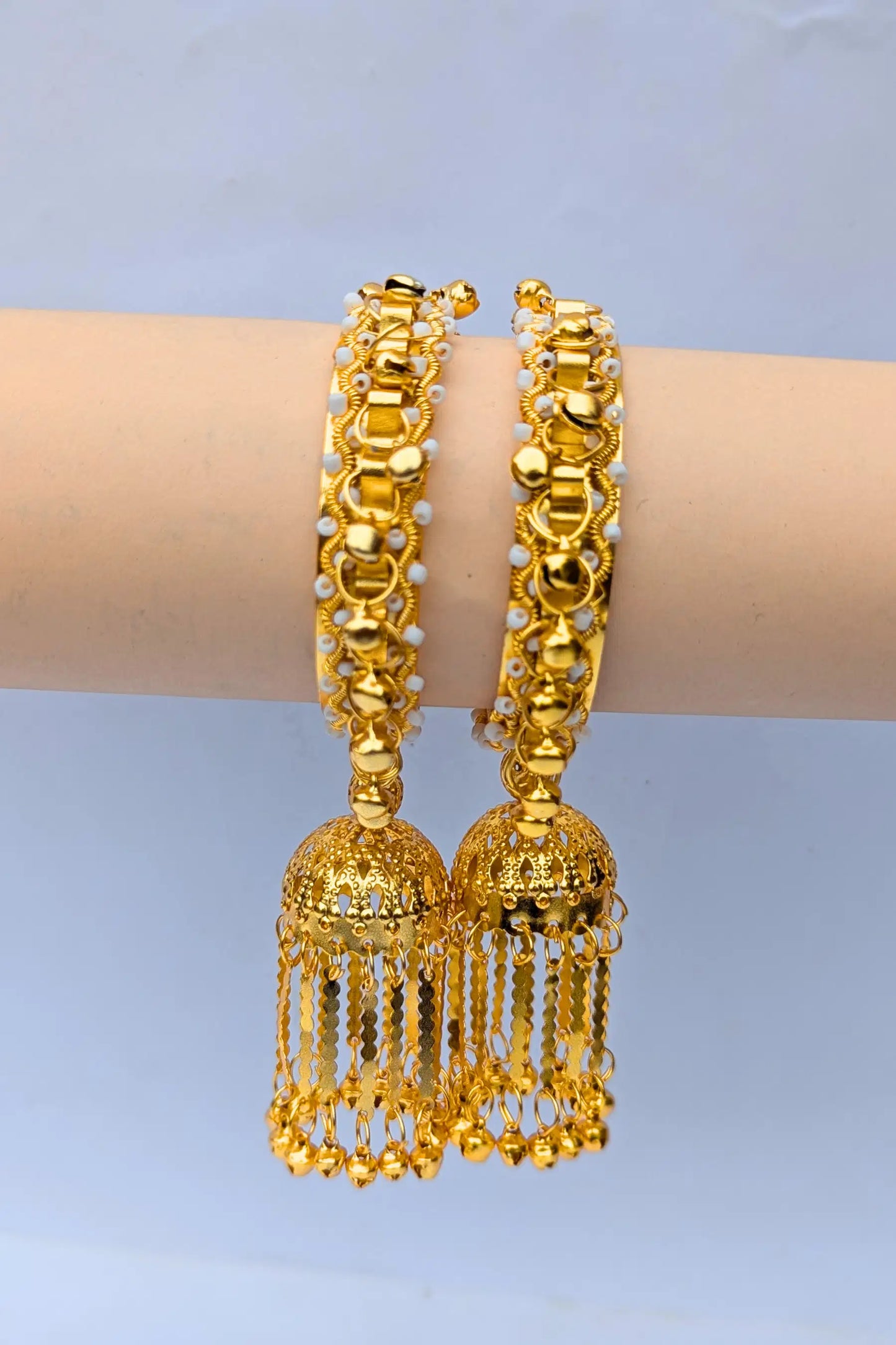 Golden bangles with tassels on a mannequin arm against a light blue background