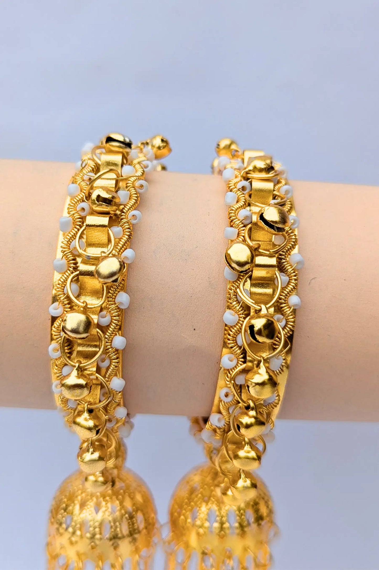 Gold bangles with white beads on a light blue background