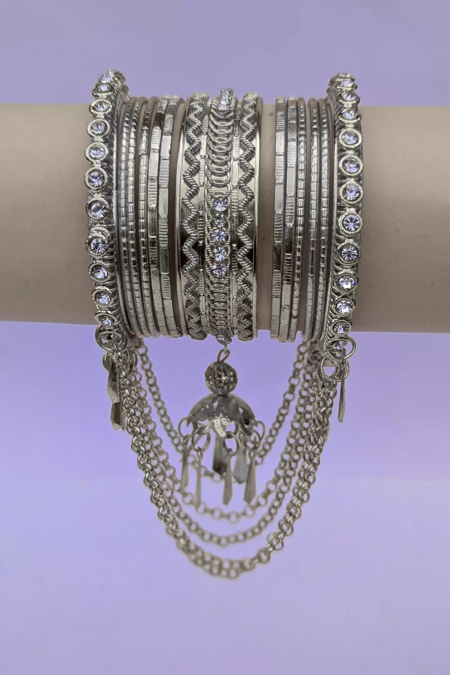 Multiple silver bracelets with intricate designs and chains on a light purple background