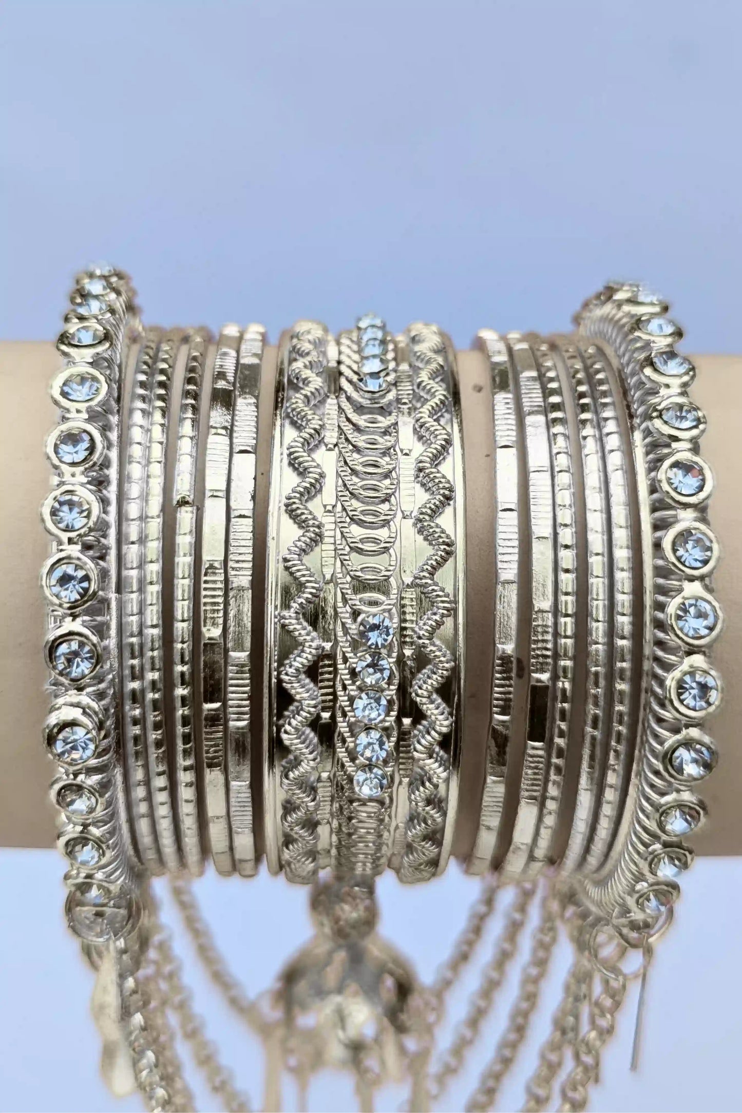 Stack of silver bangles with intricate designs on a light blue background