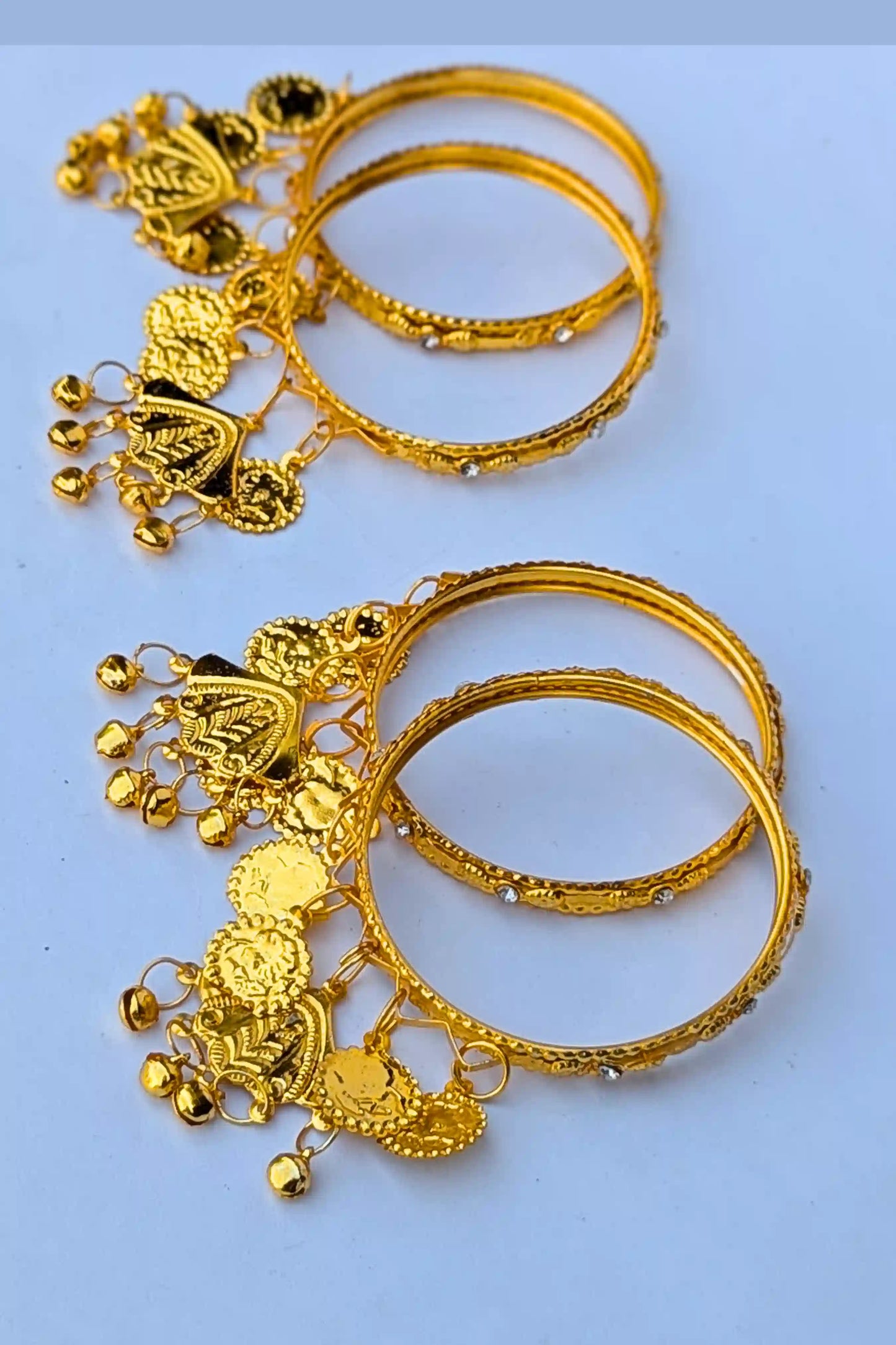 Pair of gold bangles with intricate designs on a light blue background