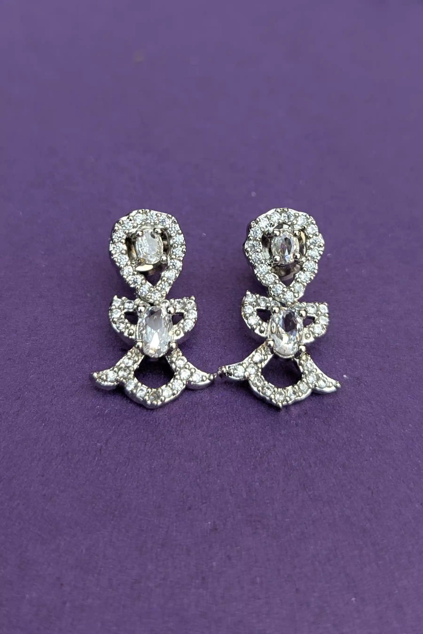 Pair of silver bow-shaped earrings with clear stones on a purple background