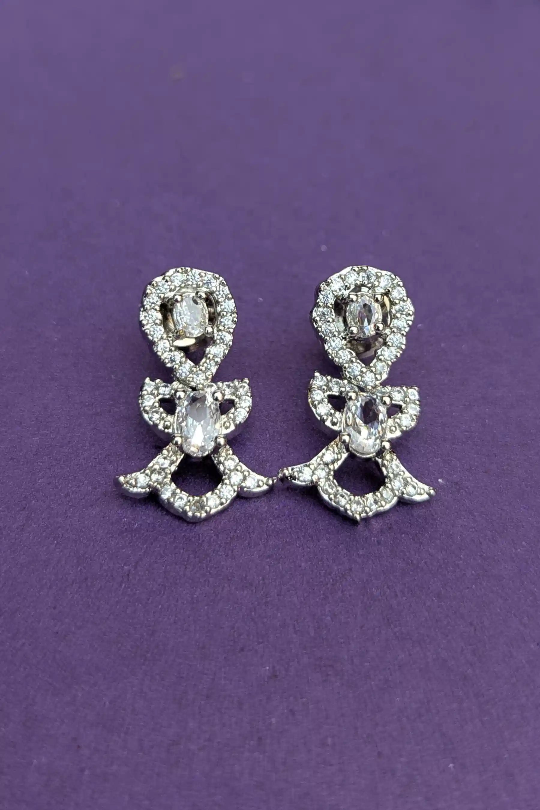 Pair of silver bow-shaped earrings with clear stones on a purple background