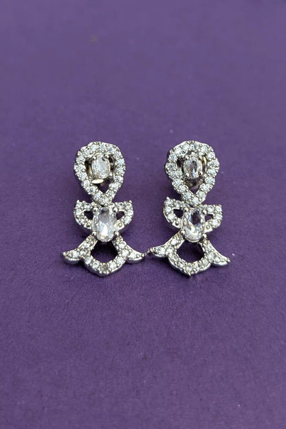 Pair of silver bow-shaped earrings with clear stones on a purple background