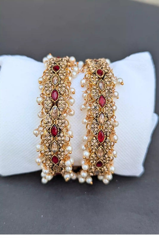 Pair of gold and red beaded bangles on a white cushion with a gray background