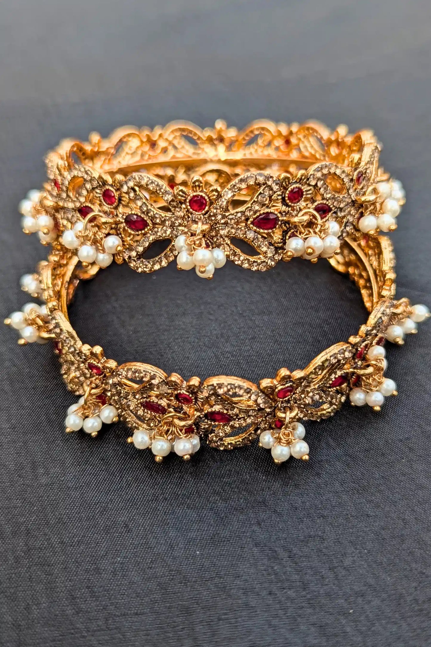 Golden bracelet with red stones and pearls on a dark background