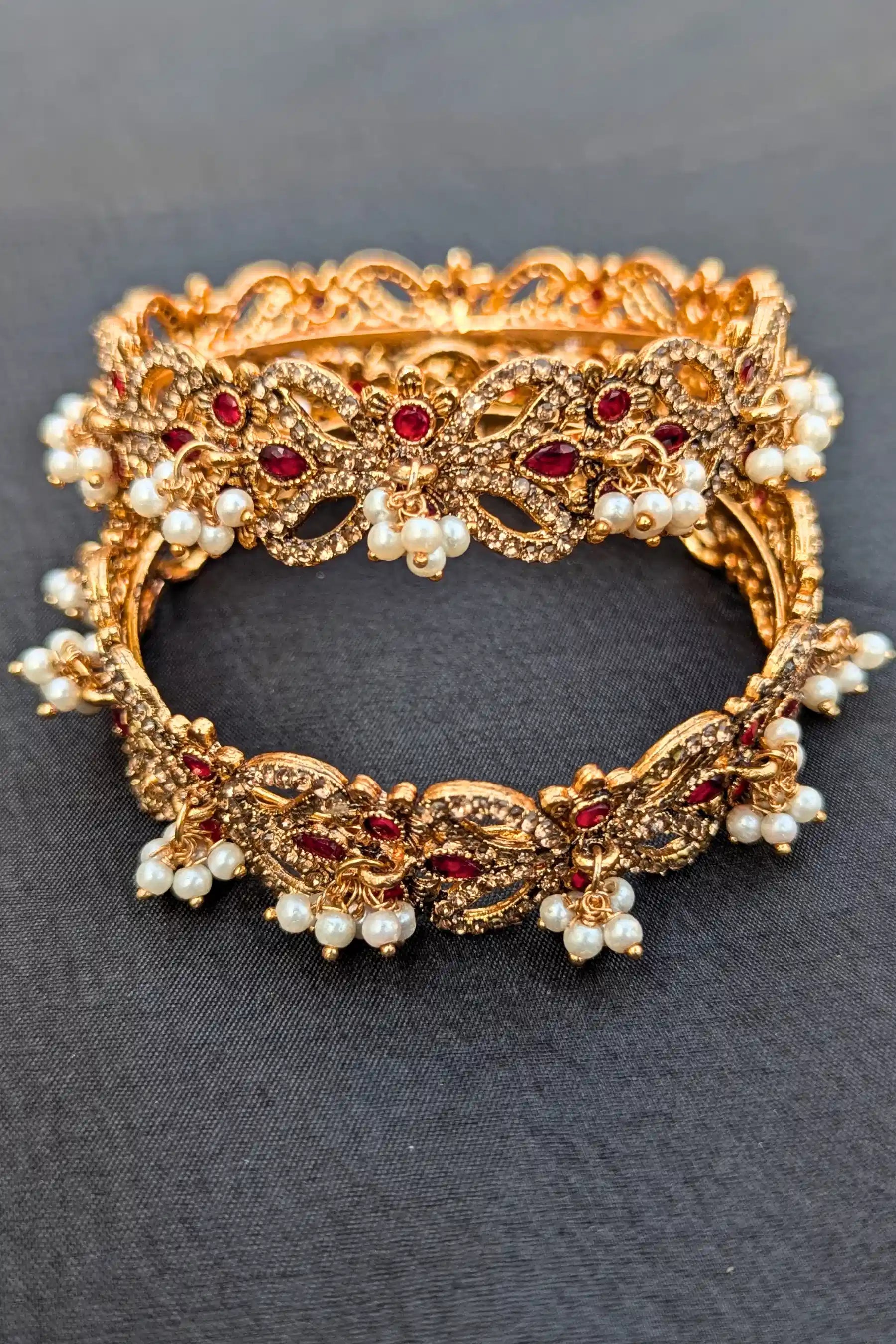 Golden bracelet with red stones and pearls on a dark background
