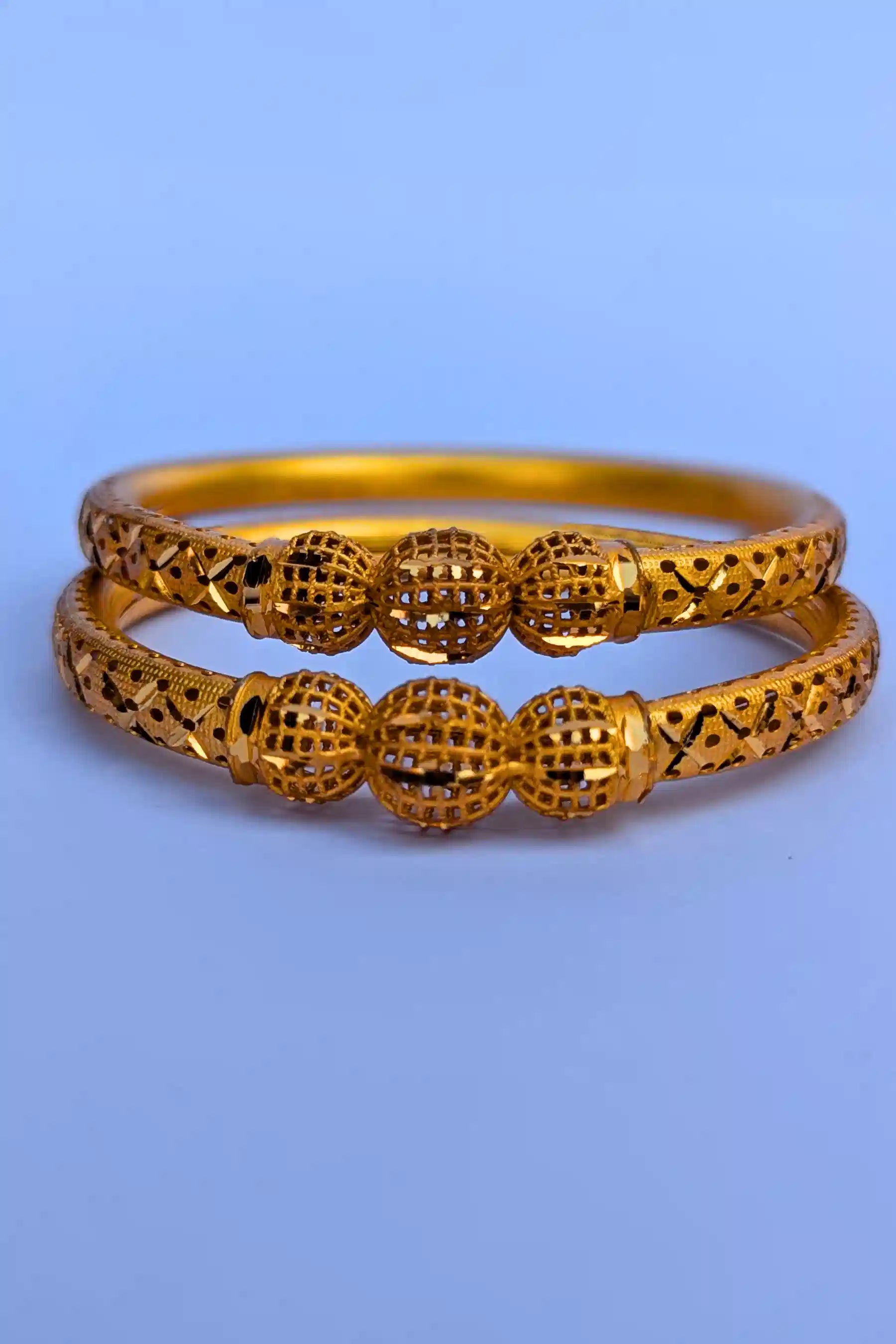 Two gold bangles with intricate designs on a blue background