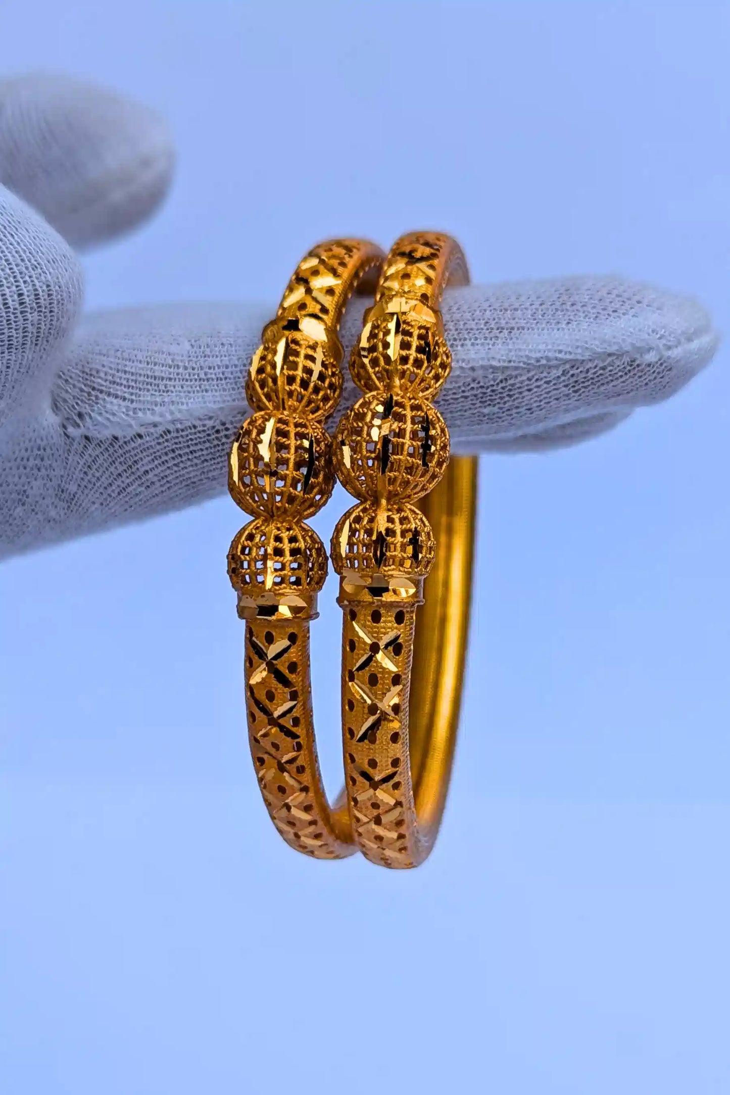 Gold bangles held by a gloved hand against a blue background