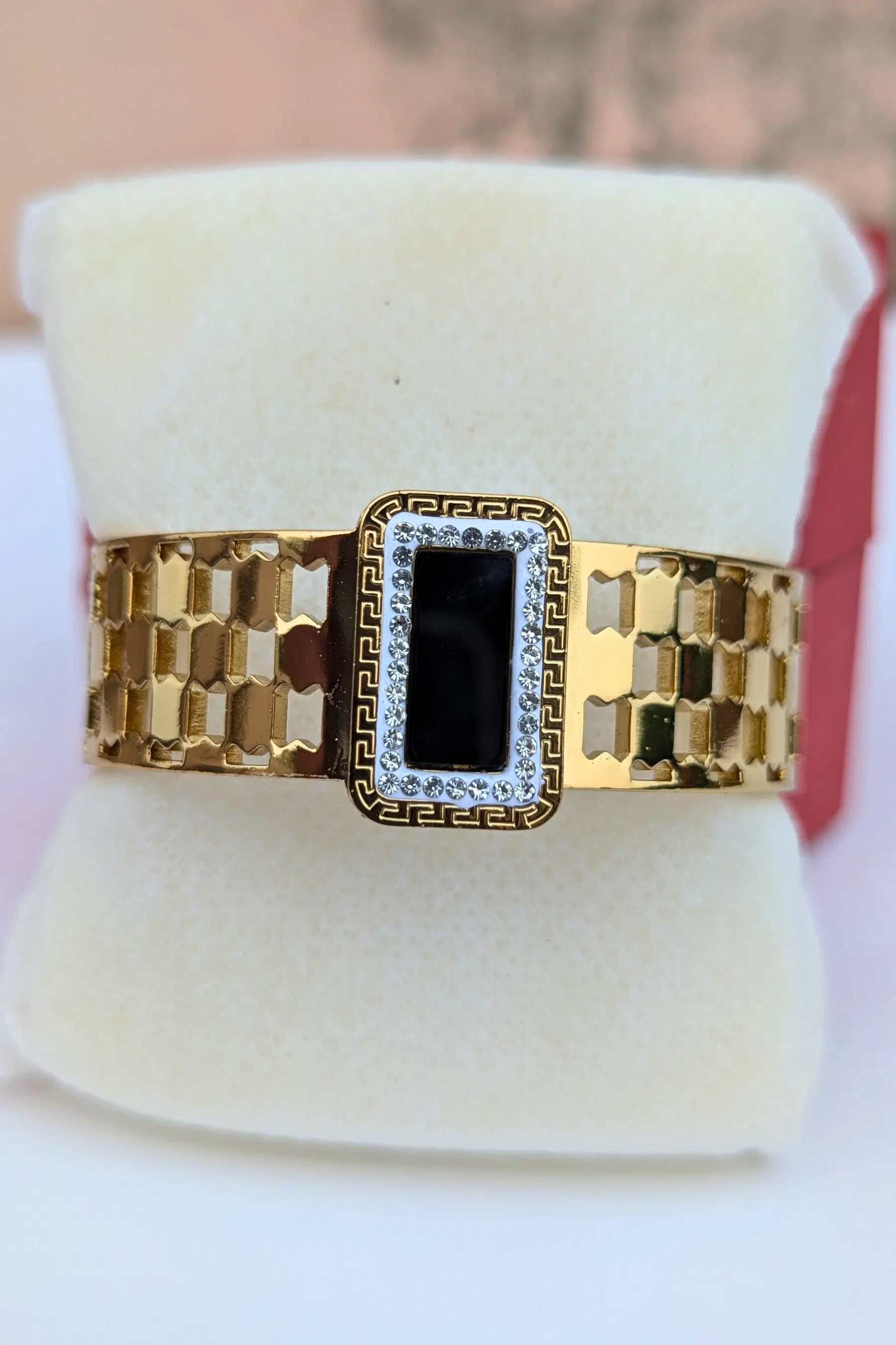 Gold ring with black center and diamond accents on a white stand.