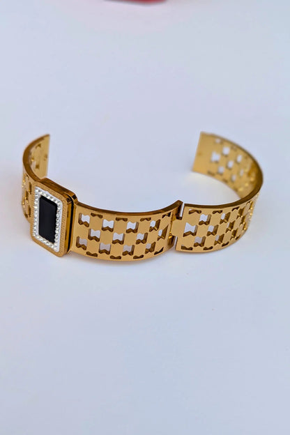 Gold bracelet with a black square inset on a light gray background