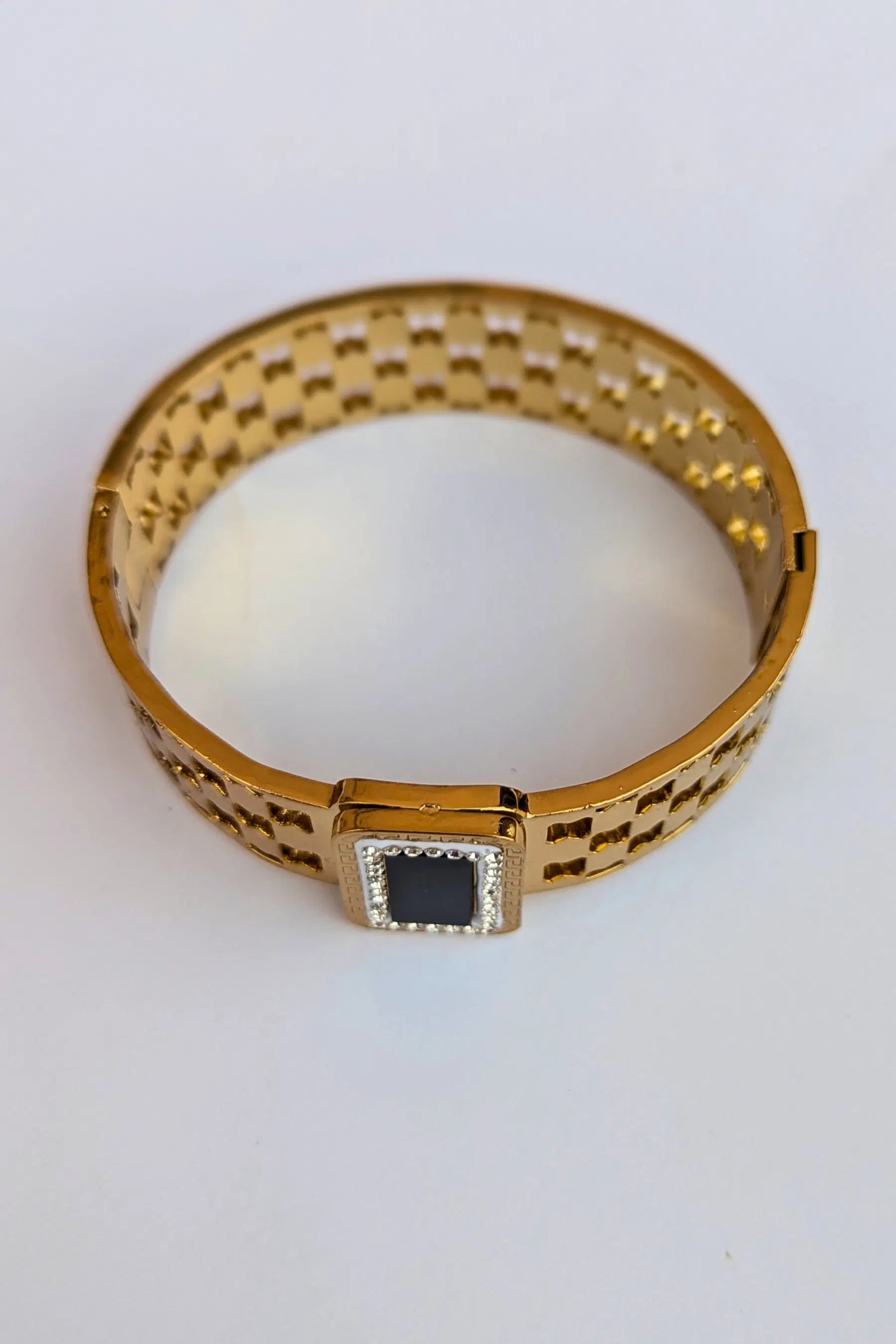 Gold bracelet with a black square stone on a white background