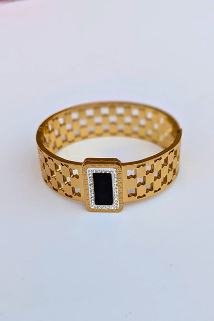 Gold bracelet with a black center on a light gray background