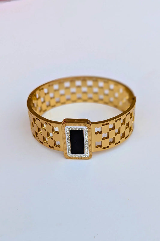 Gold bracelet with a black center on a light gray background