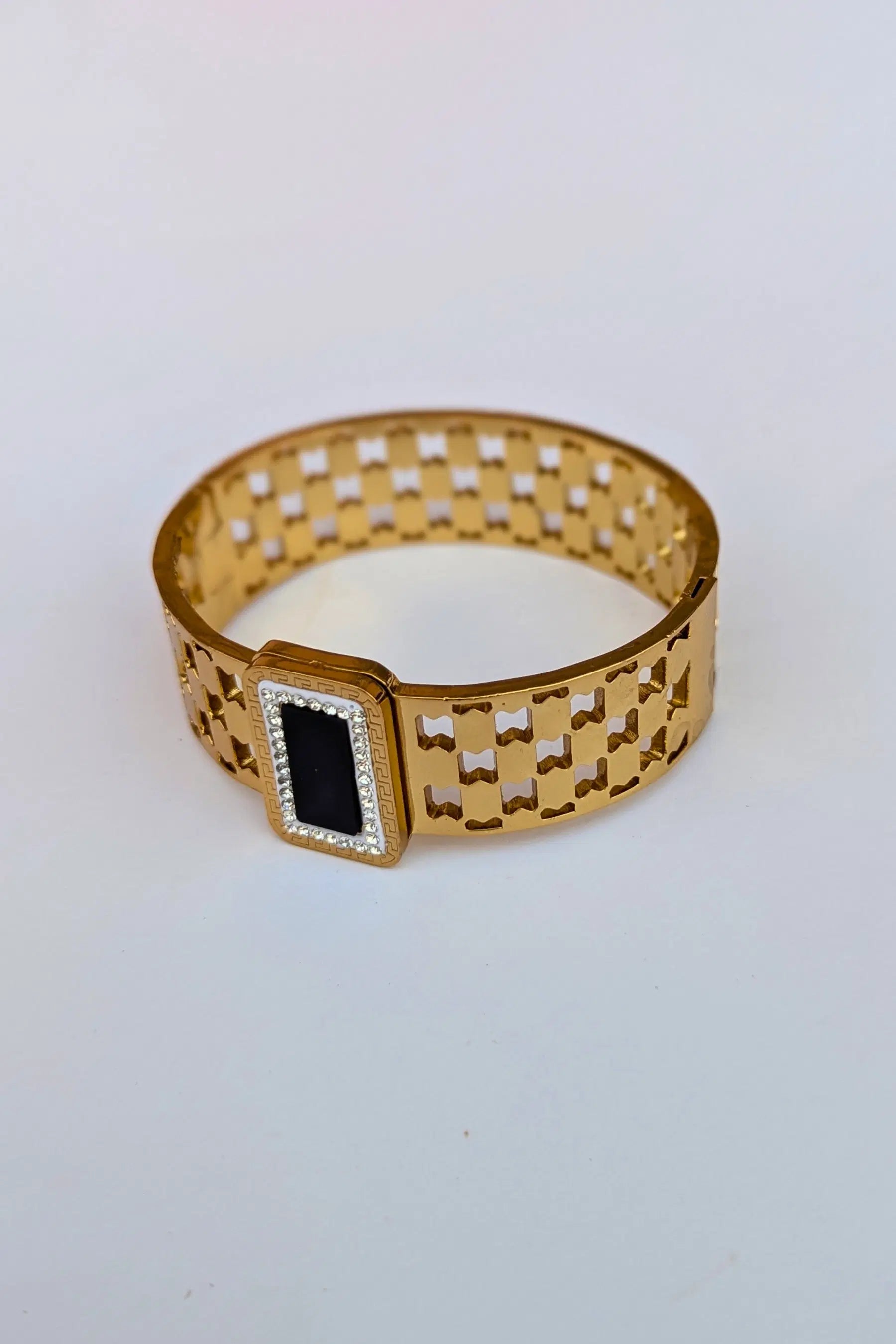 Gold bracelet with a black and white gemstone on a light gray background