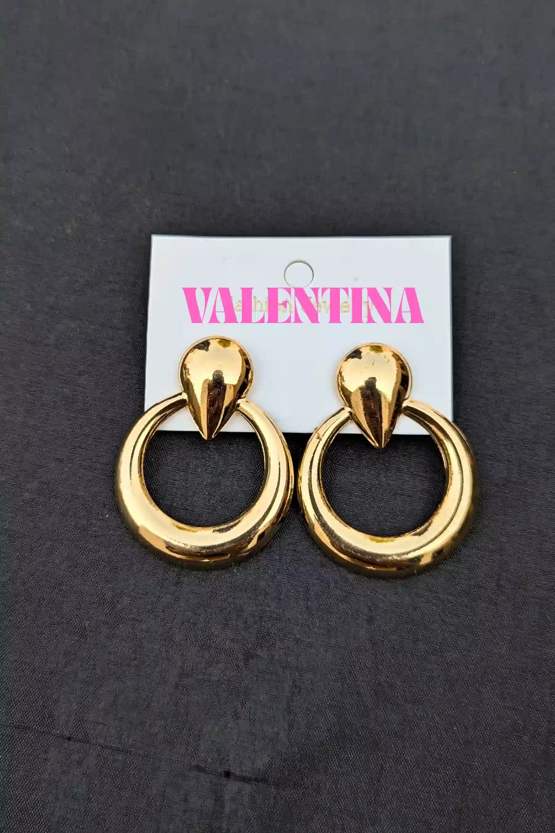 Gold hoop earrings on a Valentina branded card against a dark background