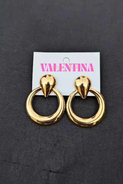Gold hoop earrings on a Valentina branded card against a dark background