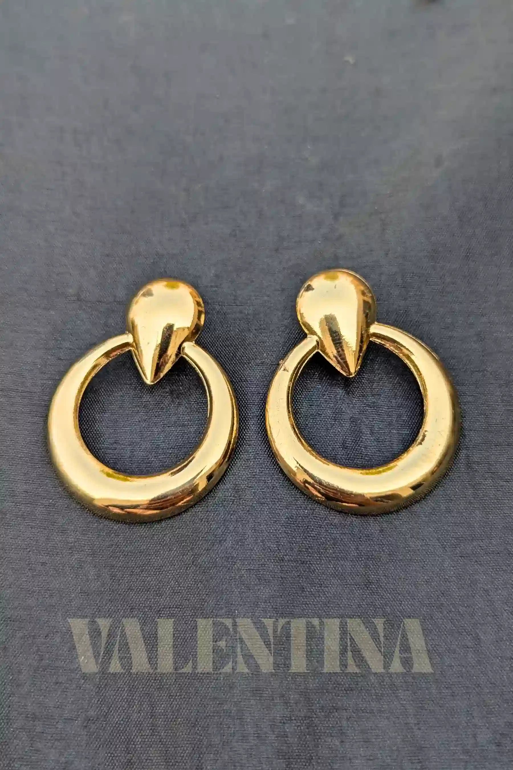 Gold hoop earrings on a dark gray background with 'Valentina' branding.