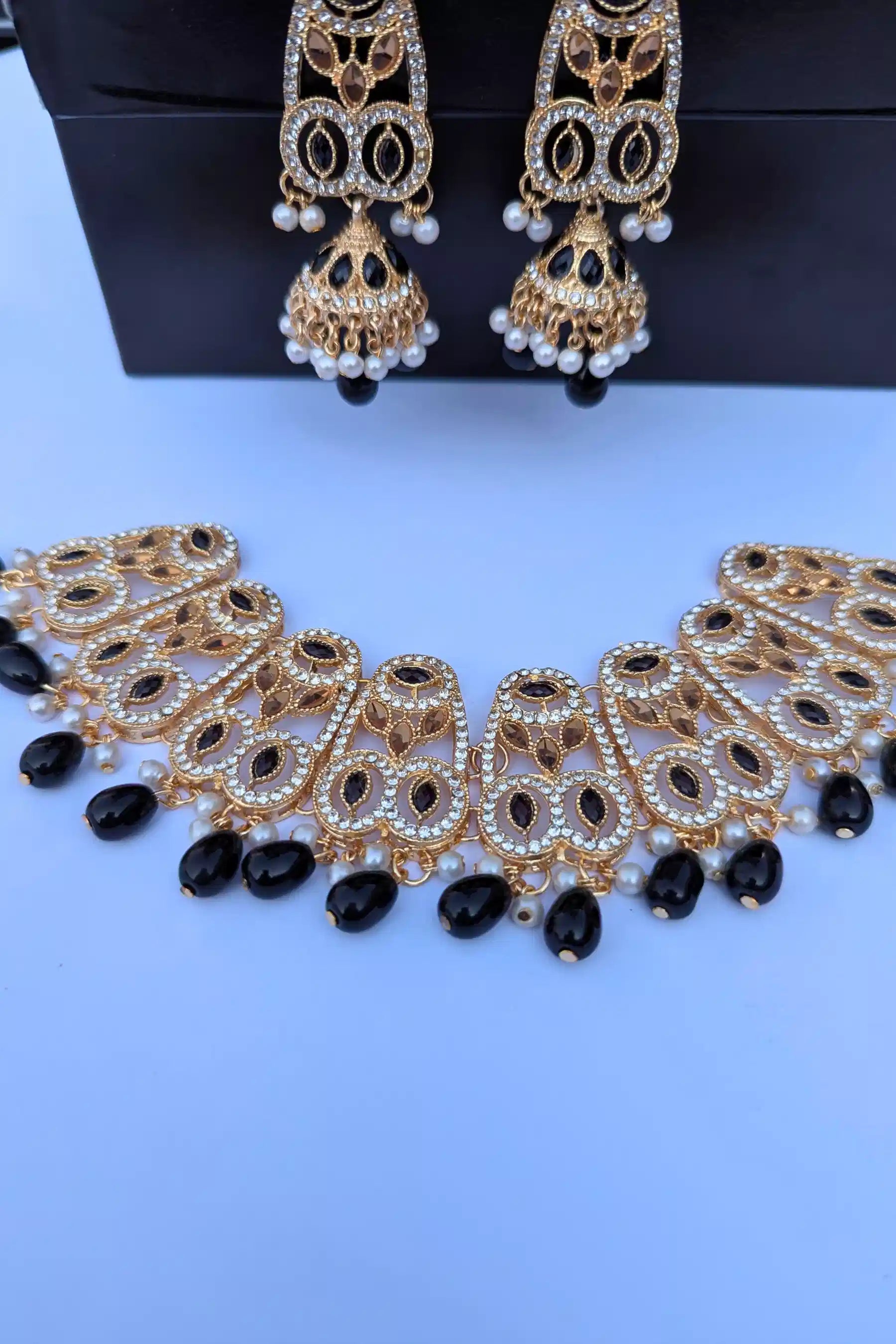 Set of gold and black jewelry including a necklace and earrings on a white background.