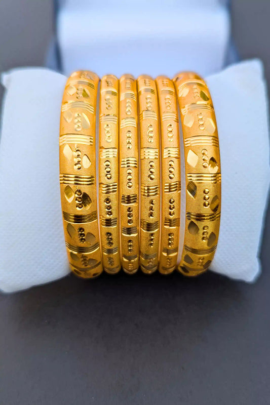 Set of gold bangles on a white cushion with a gray background