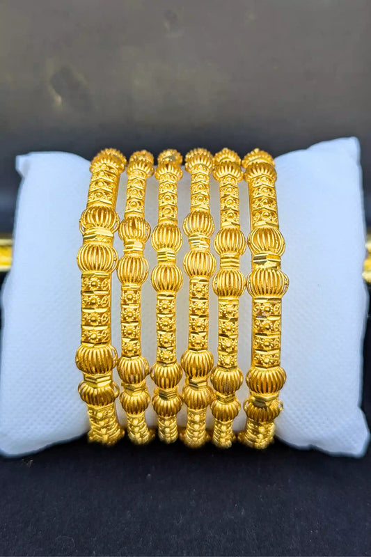 Set of gold bangles on a white cushion with a dark background