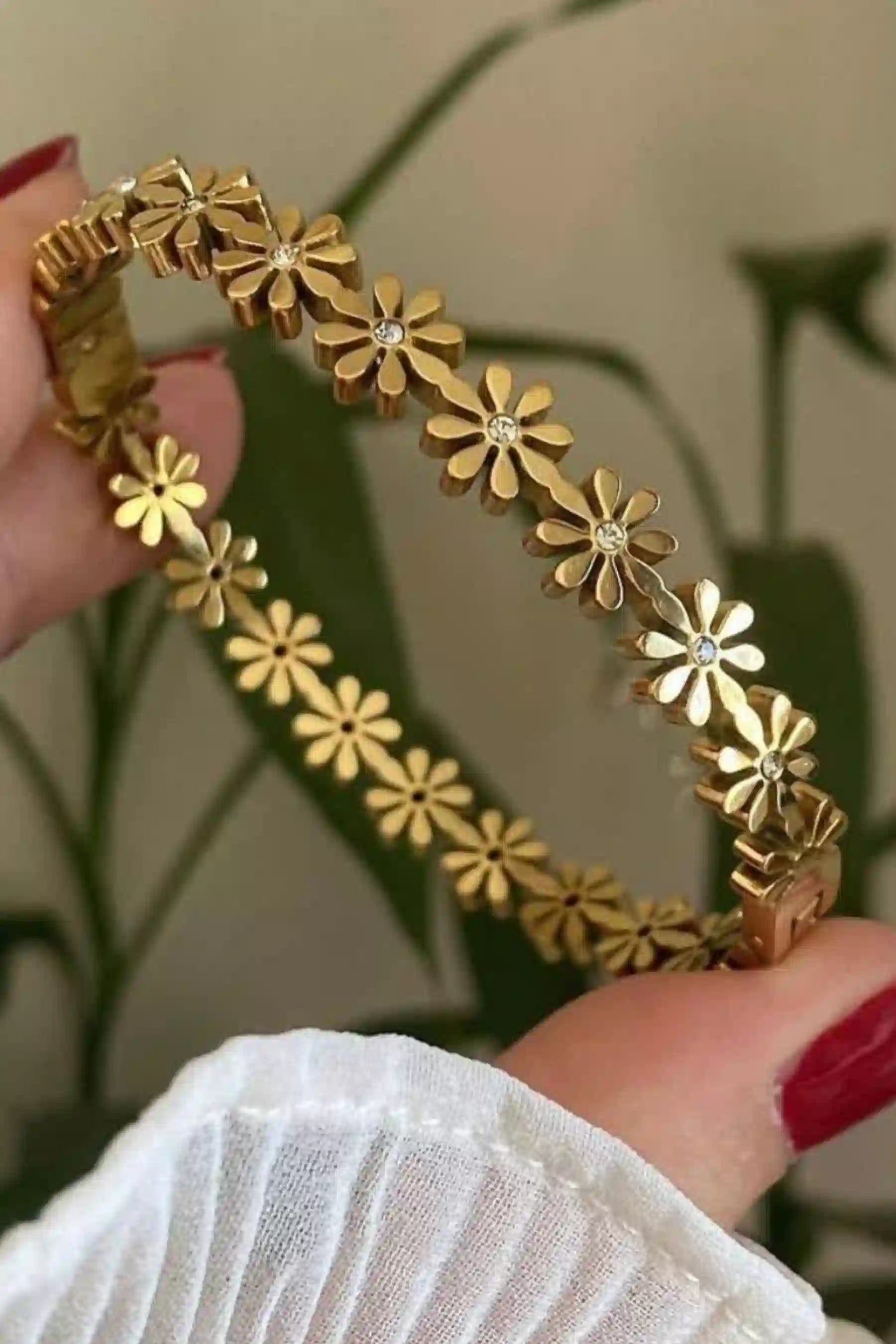 Gold floral bracelet held by a hand with red nail polish against a blurred background