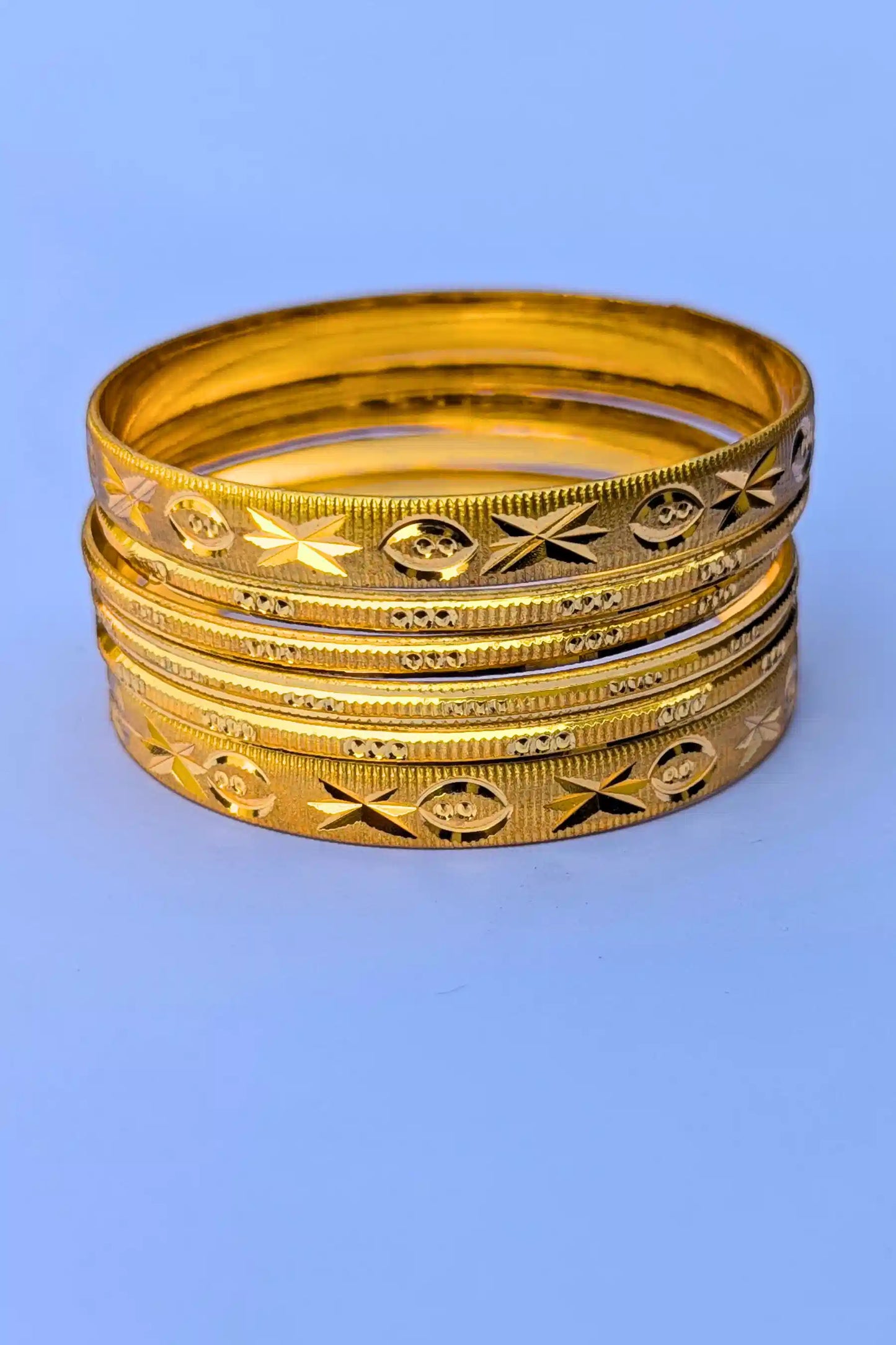 Stack of gold bangles with intricate designs on a blue background