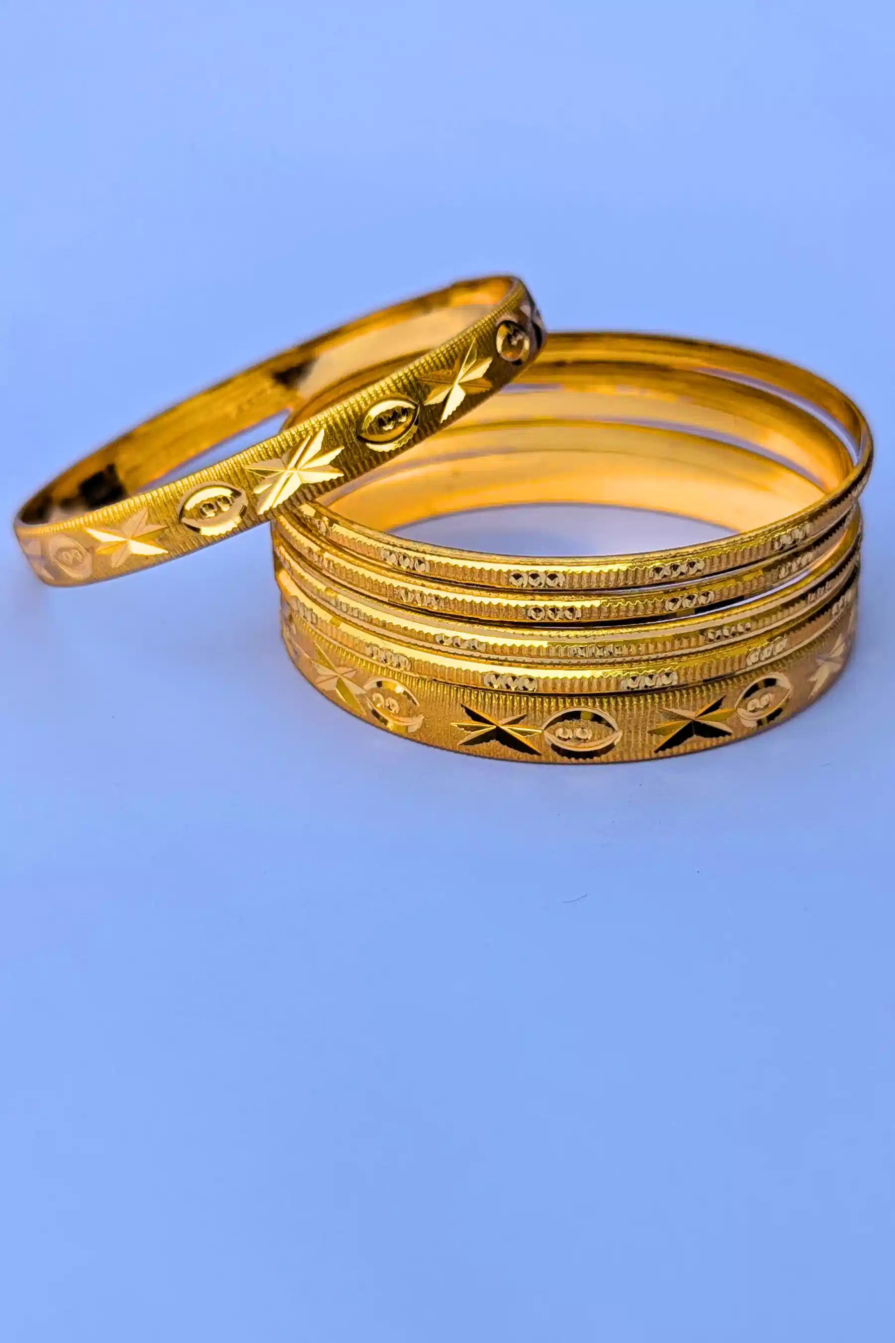 Set of gold bangles with intricate designs on a blue background