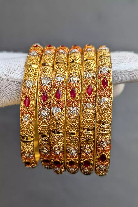 Set of gold bangles with red stones on a gray background