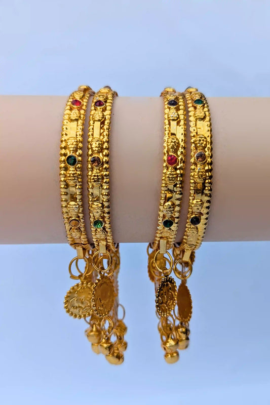 Pair of gold bangles with gemstones on a blue background