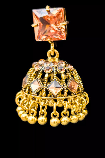 Gold jhumka earring with pink gemstone on a black background